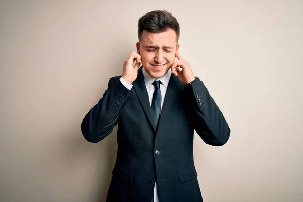 エレガントなスーツを着た若いハンサムなビジネスマンが 大きな音楽のノイズのためにいらいらする表情で指で耳を覆う孤立した背景の上にネクタイをしています ろう者の概念 — ストック写真