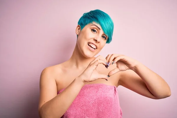 ピンクを背景に手でハートのシンボルと形状を示す愛に笑みを浮かべてシャワーの後にタオルを身に着けている青いファッションの髪を持つ若い女性 ロマン主義 — ストック写真
