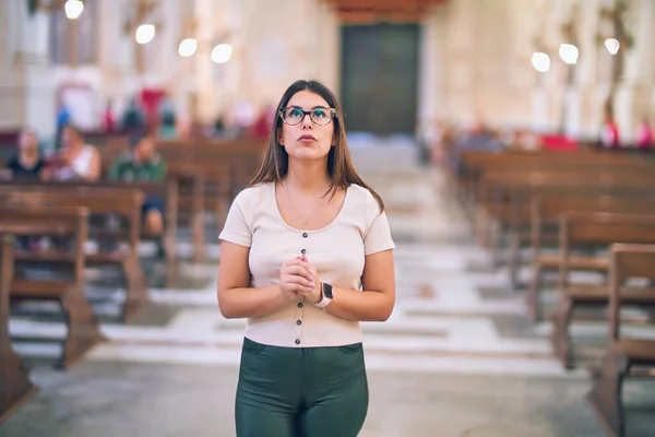 Young beautiful woman standing with hands together praying at church