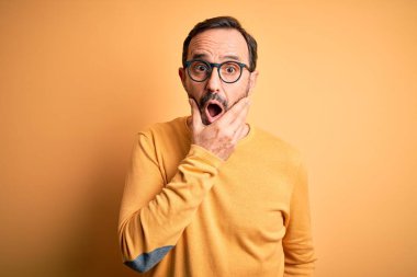 Orta yaşlı, beyaz bir adam, sarı arka planda gözlüklü, sıradan bir süveter giyiyor. İnançsızlığa, şaşkınlığa ve elleri çenesinde olan şaşkınlık ifadesine hayran görünüyor.