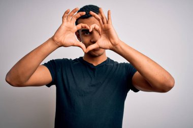 Beyaz arka planda duran, elleri ve parmaklarıyla gülümseyen, gündelik tişörtler giyen Afro-Amerikan genç adam.