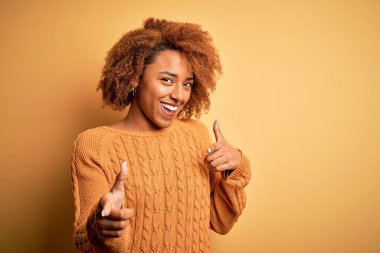 Kıvırcık saçlı, sıradan süveter giyen, mutlu ve komik yüzlü genç, güzel Afro-Amerikan kadın kamerayı işaret ediyor. İyi enerji ve titreşimler.