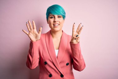 Mavi saçlı, pembe arka planda ceket giyen genç ve güzel iş kadını sekiz numaralı parmaklarıyla gülümseyerek kendinden emin ve mutlu görünüyor..