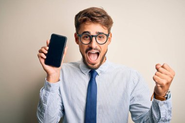 Akıllı telefonu elinde tutan genç iş adamı beyaz arka planda gururla bağırıyor ve zaferi ve başarıyı kutluyor. Çok heyecanlı, coşkulu bir duygu.