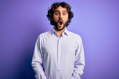 Mor arka plan üzerinde duran sakallı yakışıklı iş adamı şaşkınlık ve şaşkınlık dolu bir ifade, korku ve heyecan dolu bir yüz..