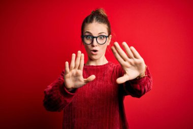 Güzel, kızıl saçlı bir kadın izole edilmiş kırmızı arka plan üzerine gündelik süveter giyip avuç içi hareketlerini durduruyor, kızgın ve hayal kırıklığına uğramış bir ifade takınıyor.