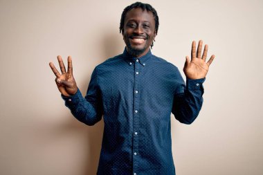 Beyaz arka plan üzerinde duran ve 8 numaralı parmaklarıyla gülümseyerek mutlu ve kendinden emin gülümseyen Afro-Amerikalı genç adam..