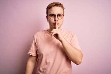 Genç, kızıl saçlı, günlük tişört giyen, izole edilmiş pembe arka planda duran ve sessiz olmak isteyen genç bir adam. Sessizlik ve gizli konsept.