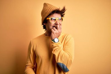 Rahat tişört ve gözlük takan genç yakışıklı adam izole edilmiş sarı arka planda gergin ve gergin görünüyor ve elleri ağızdan tırnak yiyor. Endişe sorunu.