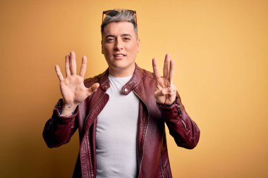 Sarı arka planda moda deri ceketi ve güneş gözlüğü takan genç ve yakışıklı bir adam sekiz numaralı parmaklarıyla gülümseyerek kendinden emin ve mutlu bir şekilde onu işaret ediyor..