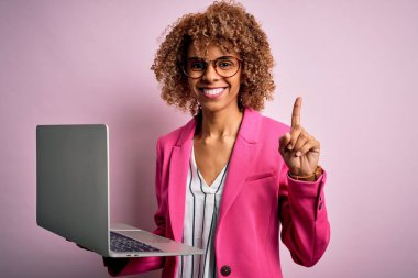 Kıvırcık saçlı, pembe arka planda dizüstü bilgisayar kullanan Afro-Amerikan iş kadını bir fikir ya da soru işareti ile şaşırdı.