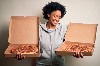 Genç, güzel afro-amerikan afro kadın mutlu ve güvenle gülümsüyor. Yüzünde tebessümle durarak kutular dolusu İtalyan taze pizzasıyla izole beyaz arka planda.