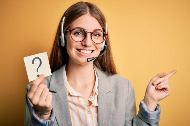 Genç kızıl saçlı çağrı merkezi ajanı, elinde soru işareti olan kulaklık kullanıyor. Elin ve parmağın yanda olduğu için çok mutlu.