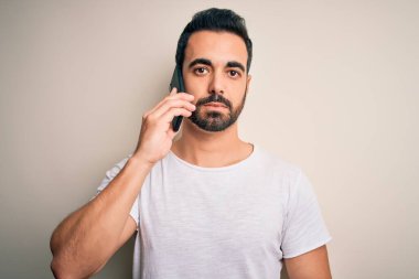 Sakallı genç yakışıklı adam akıllı telefonda konuşuyor. Akıllı bir yüz ifadesiyle ciddi düşünüyor.