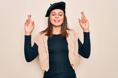 Genç, güzel, esmer bir kadın beyaz arka plan üzerine Fransız beresi takmış umut ve gözleri kapalı gülümseyerek el sallıyor. Şans ve batıl inanç..