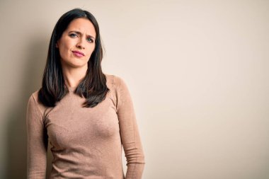 Mavi gözlü genç esmer kadın izole edilmiş beyaz arka planda günlük süveter giyiyor. Uykulu ve yorgun görünüyor. Yorgun ve akşamdan kalma, tembel gözlü..