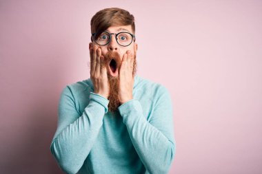 Pembe soyutlanmış arka planda gözlük takan yakışıklı kızıl saçlı, korkmuş ve şok olmuş, şaşırmış ve şaşırmış bir halde yüzü olan yakışıklı bir adam.