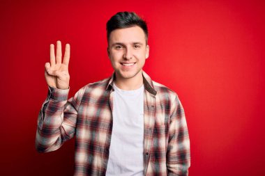Kırmızı izole edilmiş arka plan üzerine gündelik modern tişört giyen yakışıklı beyaz adam üç numarayı gösterirken kendinden emin ve mutlu bir şekilde gülümsüyor..