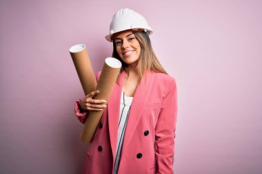 Genç, güzel esmer mimar kadın kaskını takmış elinde gülen bir yüzle ayakta duran ve gülümseyerek dişlerini gösteren planlar tutuyor.