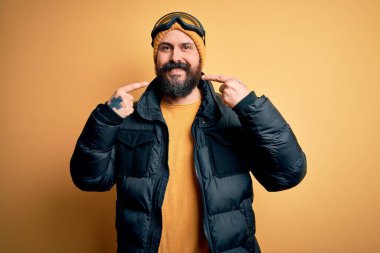 Sakallı, kar maskesi takmış, kar maskesi takmış, kayak yapan yakışıklı, kel bir kayakçı. Gülümseyen, parmakları, dişleri ve ağzı olan. Diş sağlığı konsepti.