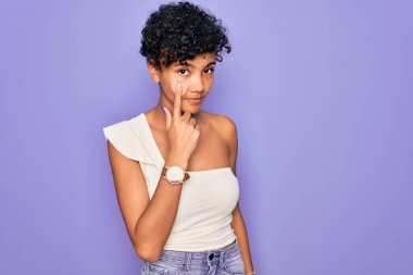 Güzel, Afro-Amerikan Afro-Amerikan bir kadın. Mor arkaplan üzerine gündelik tişört giymiş. Gözlerine bakarak jestini ve şüpheli ifadeni gösteriyor.