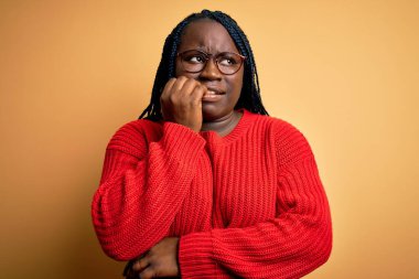 Sarı arka planda sıradan süveter giyen Afrikalı Amerikalı kadın elleri ağız yiyen tırnaklarla gergin ve stresli görünüyor. Endişe sorunu.