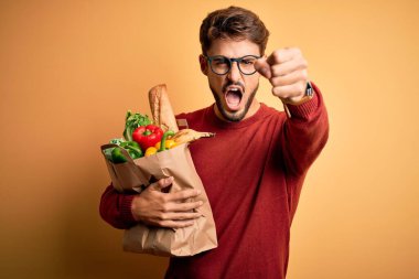 Gözlüklü genç adam elinde yiyecek dolu bir torba tutuyordu. Sinirli ve sinirli bir şekilde bağırıyordu. Öfkeyle bağırıyordu.