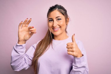 Genç, güzel bir kadın pembe izole edilmiş arka planda Fransız pastası yiyor. Kocaman gülümsüyor. İşaret veriyor.