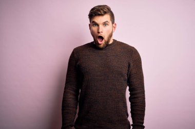 Sakallı ve mavi gözlü genç bir adam pembe arka planda sıradan bir süveter giyiyor. Korkuyor ve şok geçiriyor..