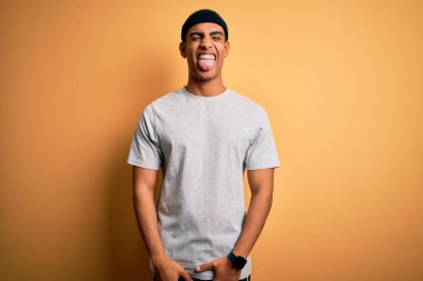 Sarı arka plan üzerine spor giysili yakışıklı Afro-Amerikan sporcusu komik bir ifadeyle dilini dışarı çıkartıyor. Duygu kavramı.