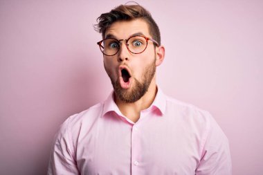 Sakallı, mavi gözlü, pembe tişörtlü, gözlüklü, korkmuş ve şok olmuş genç sarışın adam..