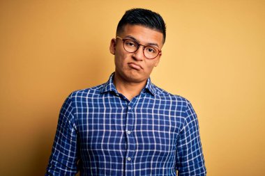 Sarı arka plan üzerine gündelik gömlek ve gözlük takan genç, yakışıklı Latin adam uykulu ve yorgun görünüyor, yorgunluktan yorgun ve akşamdan kalma, sabahları tembel gözler..