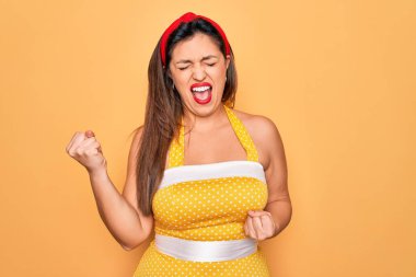 Sarı arka planda 50 'li yaşlarda moda modasına uygun seksi giyinen Latin kökenli genç bir kadın kolları havada ve gözleri kapalı bir şekilde başarıyı kutluyor ve şaşırıyor. Kazanan konsept.