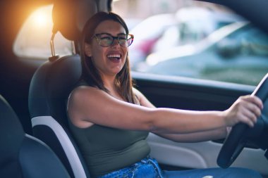 Mutlu ve kendinden emin gülümseyen genç ve güzel bir kadın. Yüzünde gülümsemeyle oturup araba sürmek.
