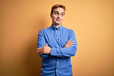 Genç, kızıl saçlı, sıradan çizgili tişörtlü, izole edilmiş sarı arka planda gülümseyen ve başka yöne bakan yakışıklı bir adam..