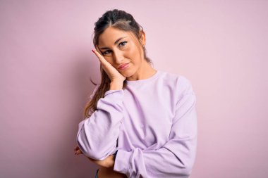 Pembe izole edilmiş arka plan üzerinde eşofman üstü giyen genç ve güzel bir bayan kollarını kavuşturarak depresyondan sıkılmış ve yorgun göründüğünü düşünüyor..