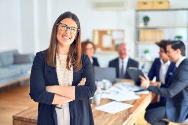Bir grup iş adamı bir toplantıda birlikte çalışırken mutlu ve kendinden emin gülümsüyor. Bir tanesi, yüzünde gülümsemeyle büroya bakıyor..