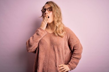 Genç, güzel, sarışın bir kadın pembe arka planda günlük süveter ve gözlük takıyor. Elle ağzını kapatmaktan sıkılmış. Huzursuz ve uykulu..