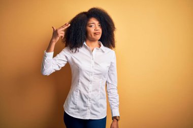 Afro saçlı, güzel, Afro-Amerikan zarif bir kadın sarı arka planda duruyor. Kendini vuruyor ve öldürüyor. Silah gibi el ve parmaklarını işaret ediyor..