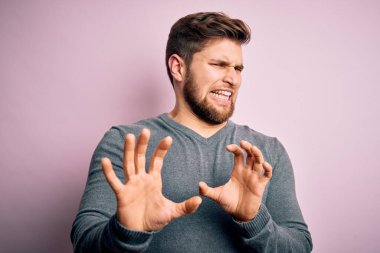 Sakallı, mavi gözlü, hoş olmayan bir süveter giyen, hoşnutsuz ve korku dolu genç sarışın adam tiksinti reaksiyonu yüzünden tiksinti ifadesi takınıyor. Eller havada