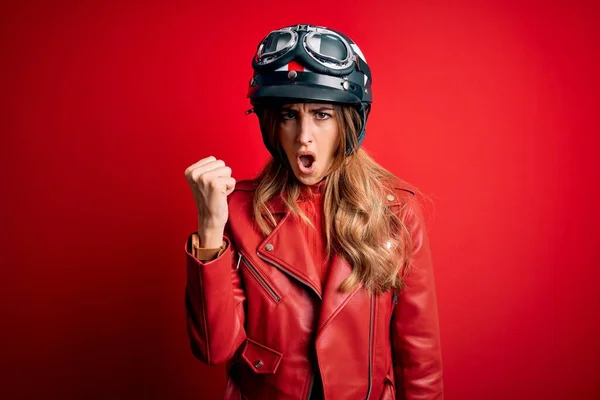 赤い背景の上に元ヘルメットを身に着けている若い美しいブルネットのオートバイの女性は怒りで叫んでいる間 怒りと怒りに苛まれ 激怒拳を上げ怒っている 激怒と積極的な概念 — ストック写真
