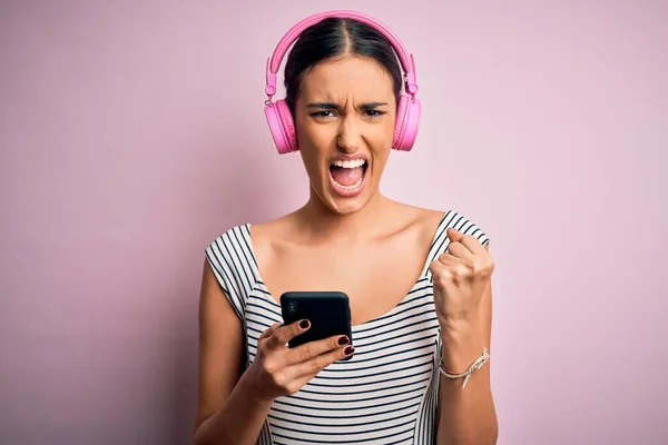 若い美しいブルネットの女性は ヘッドフォンやスマートフォンを使用して音楽を聞いていらいらし 怒りで叫び 狂気と大声で手を上げ 怒りの概念 — ストック写真