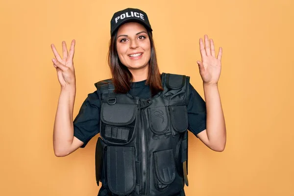 年轻美丽的黑发女警察身穿警服 头戴帽子 头戴防弹背心 手指指向八号 面带微笑 自信而快乐 — 图库照片