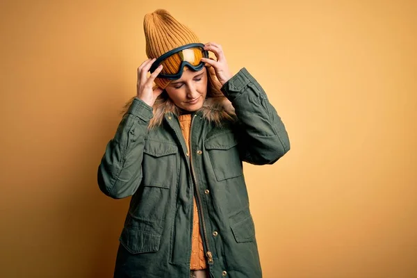 中年漂亮的金发滑雪者女人穿着雪地运动鞋和滑雪护目镜 因疼痛和偏头痛而极度头痛和紧张 手放在头上 — 图库照片