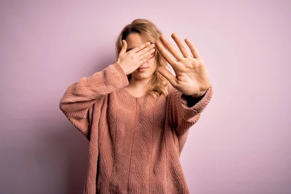 Young beautiful blonde woman wearing casual sweater and glasses over pink background covering eyes with hands and doing stop gesture with sad and fear expression. Embarrassed and negative concept.