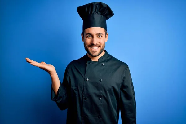年轻英俊的厨师 留着胡子 身穿炊具制服 头戴蓝色背景的帽子 笑容满面 手牵手看着相机 — 图库照片