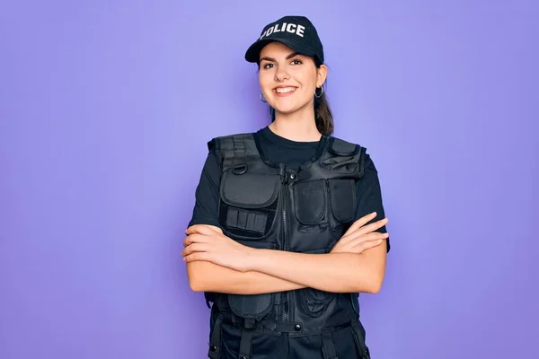年轻的女警察身穿紫色背景的防弹背心制服 面带微笑 交叉着双臂看着相机 积极的人 — 图库照片