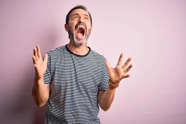 孤立したピンクの背景の上に立ったカジュアルなストライプのTシャツを着た中年のホーリーマンは狂気と怒鳴り 積極的な表情と腕を上げて叫んでいます 欲求不満の概念 — ストック写真