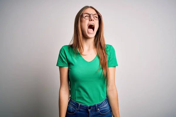 若い美しい赤毛の女性が怒って怒って怒って怒って怒って叫んで 怒りで叫んで カジュアルな緑のTシャツと眼鏡を着用 激怒と積極的な概念 — ストック写真