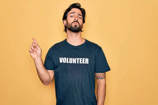 若いハンサムなパニックボランティア男性ボランティアTシャツを社会的ケアとして身に着けている広告 深刻かつ穏やかな顔を示す側に手指で指す — ストック写真